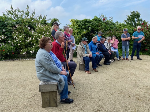 Luisteren naar het verhaal van de gids in 'de Cleyne Hortus'. De meeste deelnemers zitten op een bankje